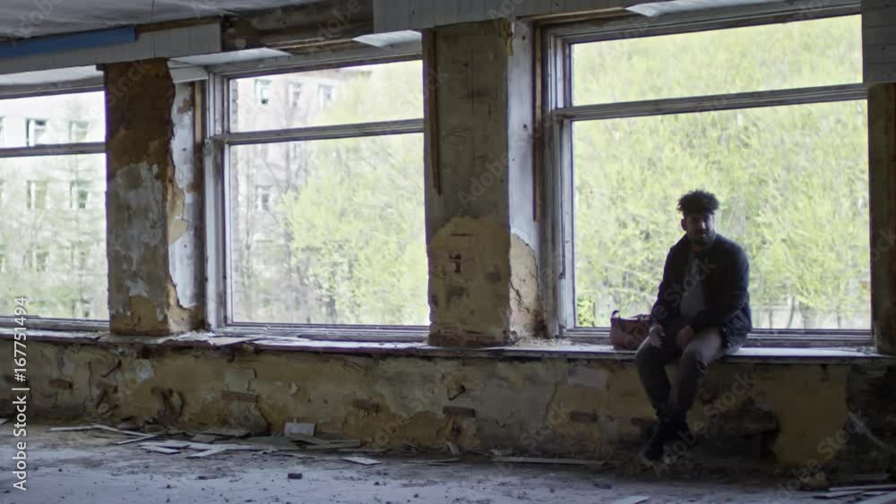 Lockdown of serious Arab man sitting on windowsill of broken window in abandoned building Lockdown of serious Arab man sitting on windowsill of broken window in abandoned building