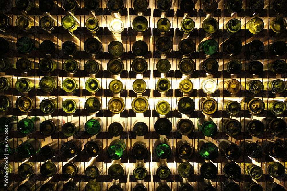 Obraz premium Many glass wine bottles on wine shelves with lighting. Interior in the restaurant. Color photo