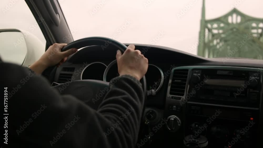 Closeup Of Young Woman's Hands On Steering Wheel, As She Drives Across Art Deco Style Bridge On A Cloudy Day In The Pacific Northwest Closeup Of Young Woman's Hands On Steering Wheel, As She Drives Across Art Deco Style Bridge On A Cloudy Day In The Pacific Northwest