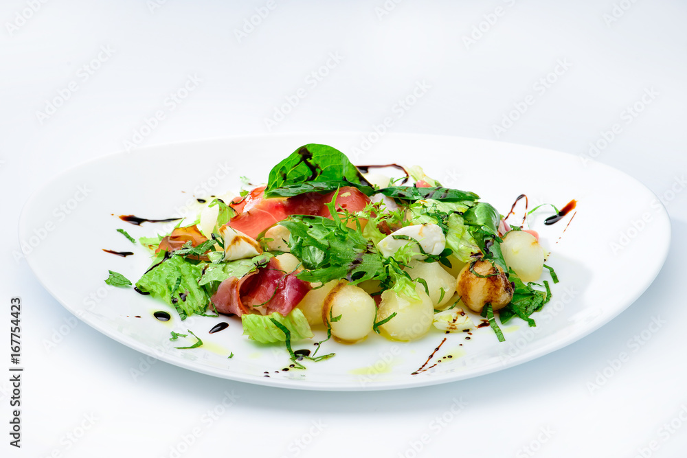 classic Italian summer delicious fresh salad with cheese, parma ham and soy sauce on white plate, on light background