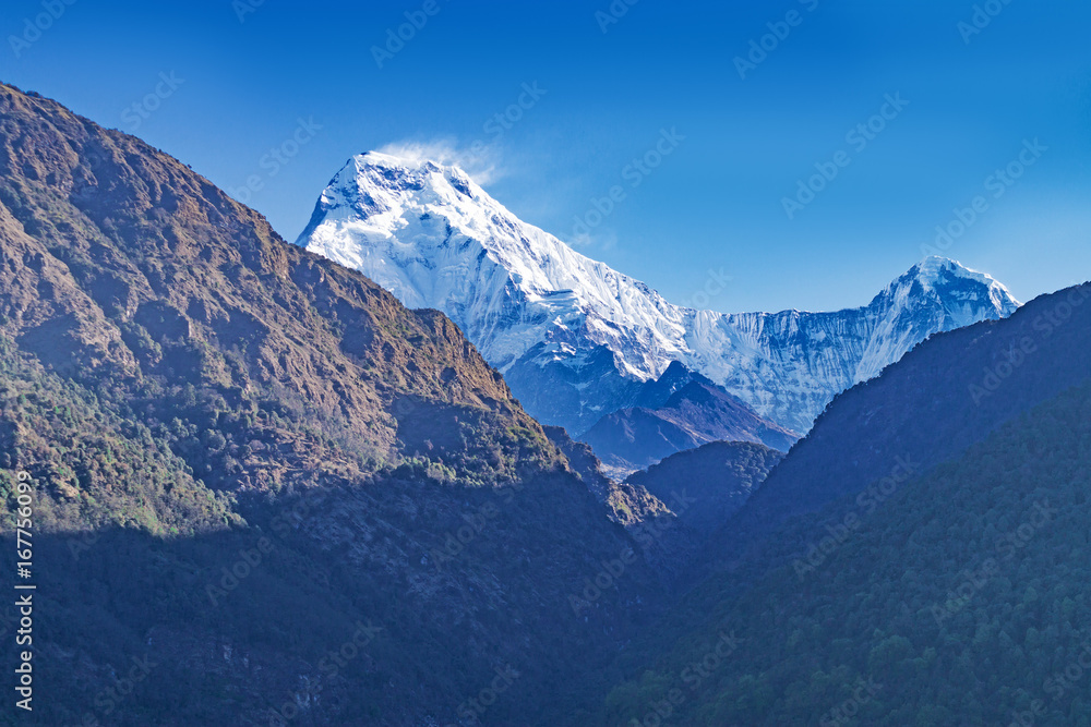 Snow-covered peak of Mount Annapurna against the background of a blue sky in the distance. Nepal.