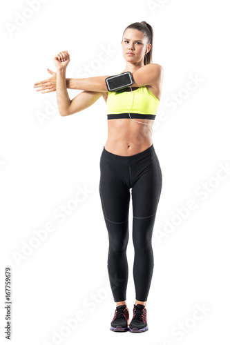 Young female jogger warming up doing shoulder exercise while stretching arm. Full body length portrait isolated on white studio background