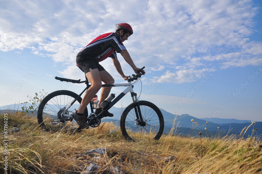 Young man riding a bike on hill under a mountain, extreme riding bicycle off road on rocks