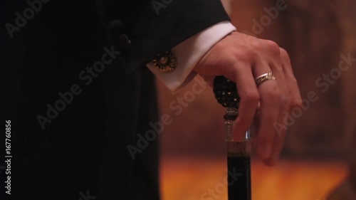 Gentleman holds a cane, a man fingering his fingers on the handle of a walking stick.
