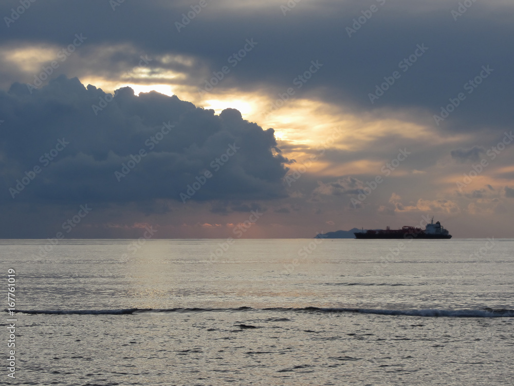 Warm sea sunset with cargo ship at the horizon . Giants cumulonimbus clouds are in the sky. Tuscany, Italy