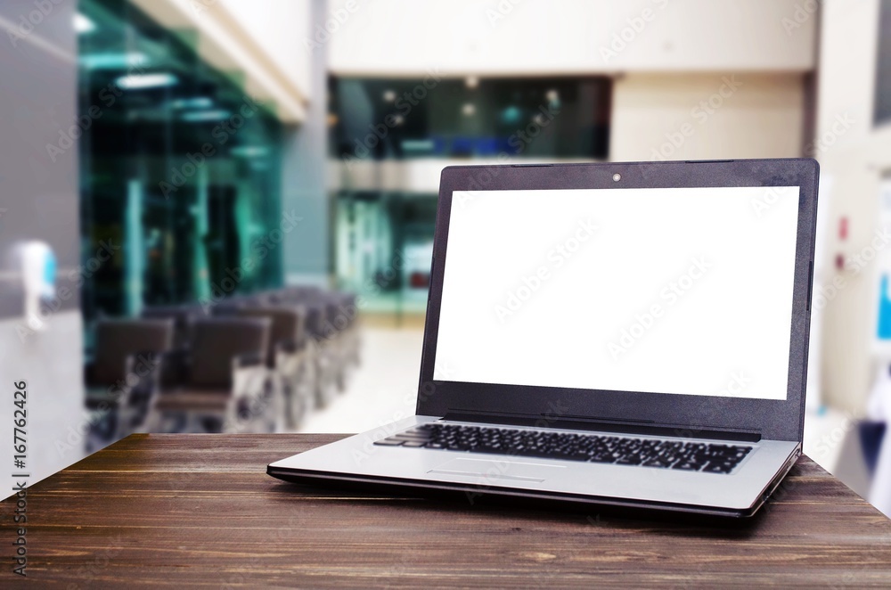 Laptop computer with white blank screen for advertising on wooden desk with blurred view of empty wheelchair in hospital, health care medical technology, working outside office, social media concept Laptop computer with white blank screen for advertising on wooden desk with blurred view of empty wheelchair in hospital, health care medical technology, working outside office, social media concept