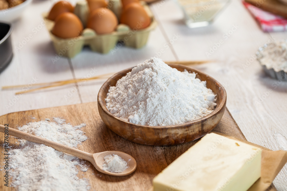 Baking ingredients in rural kitchen - dough recipe ingredients (eggs, flour, milk, butter, sugar) and rolling pin on wooden white table. Close up Baking ingredients in rural kitchen - dough recipe ingredients (eggs, flour, milk, butter, sugar) and rolling pin on wooden white table. Close up