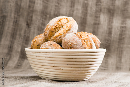 a traditional round artisan wheat bread loaves in a basket, textile background. Rustic style, shallow dof