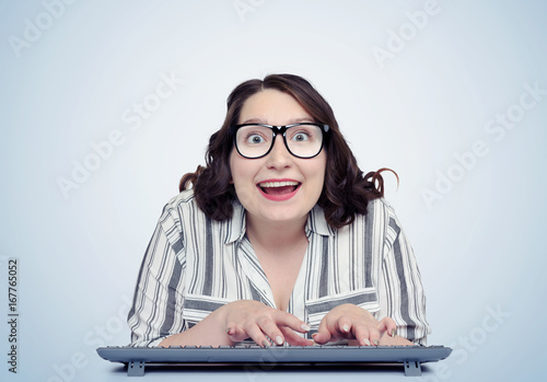 Happy funny girl programmer in glasses with keyboard in front of computer