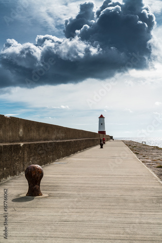 Lighthouse at the end of jetty and seawall, Berwick upon Tweed, Northumberland, England against a stormy sky