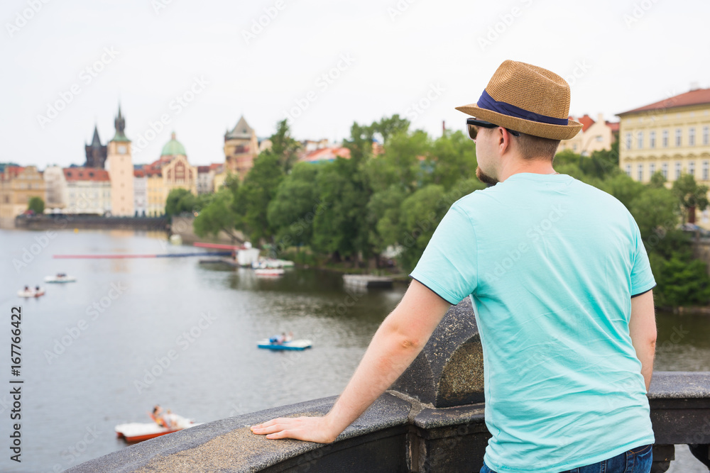 Back view of happy stylish tourist on Charles Bridge, Prague, Czech Republic. Handsome man travelling in Europe.