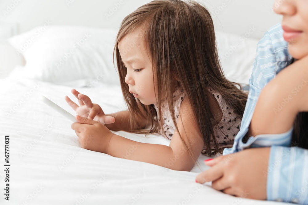 Little baby girl playing with smartphone while lying in bed Little baby girl playing with smartphone while lying in bed