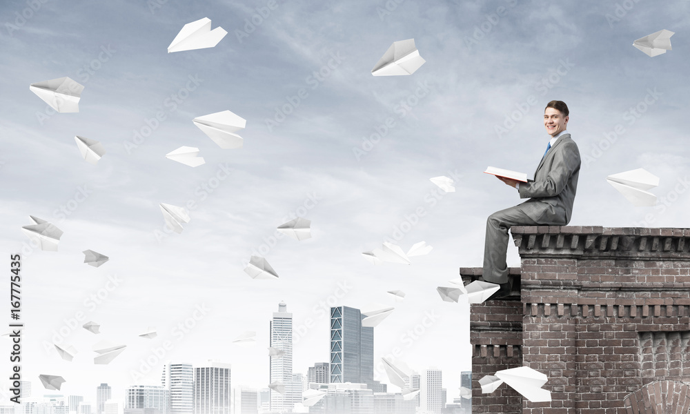 Man on roof edge reading book and cityscape at background Man on roof edge reading book and cityscape at background