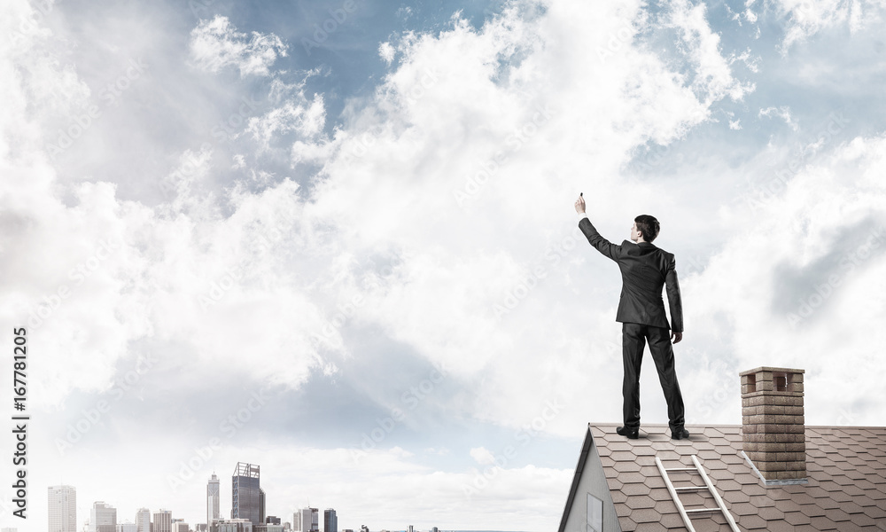 Businessman on house roof touch empty space. Mixed media Businessman on house roof touch empty space. Mixed media