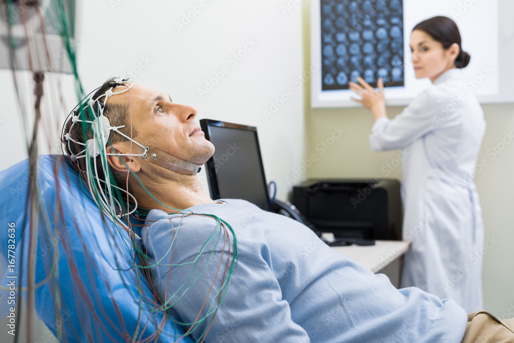 Female doctor carrying out electroencephalography of man - obrazy, fototapety, plakaty 
