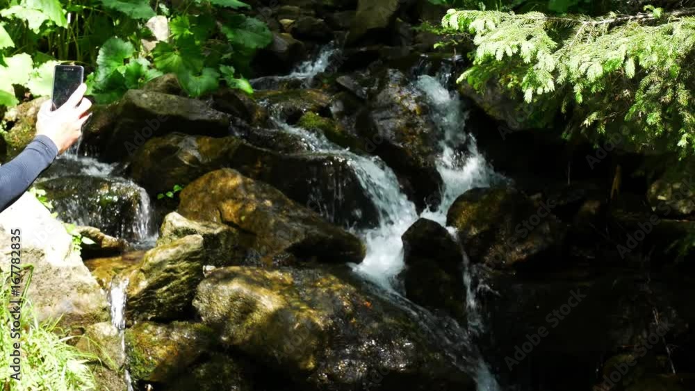 A tourist photographs a waterfall on a mobile phone. A tourist photographs a waterfall on a mobile phone.