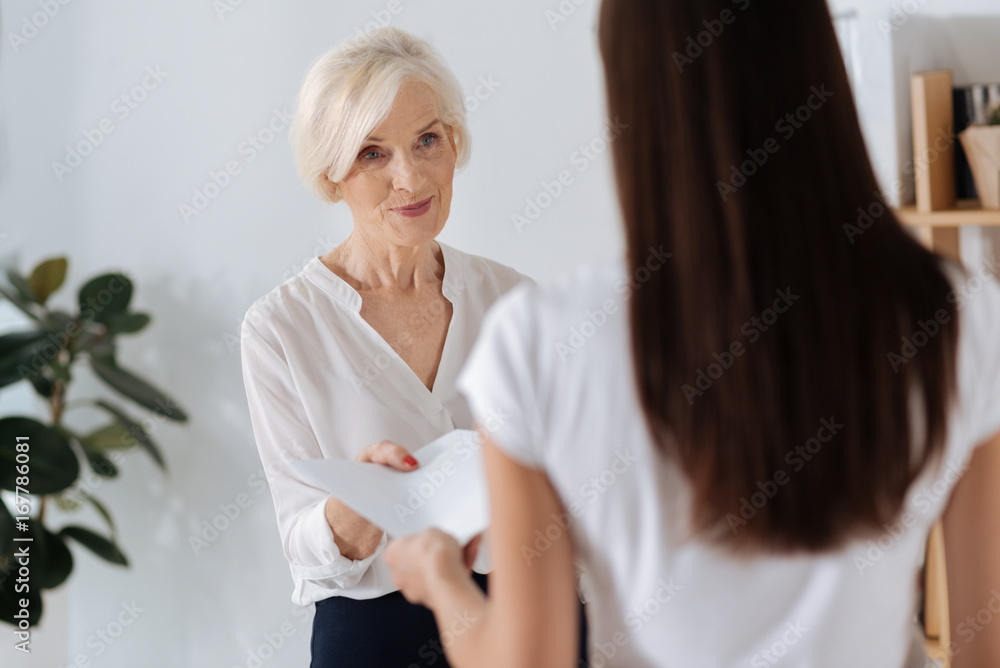 Fototapeta premium Positive smart woman giving her colleague a document