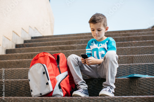 Child sitting outside school and playing games on his cell phone
