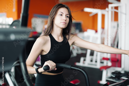 Young beautiful white girl in a sports suit is engaged on a stationary bike in the fitness club.