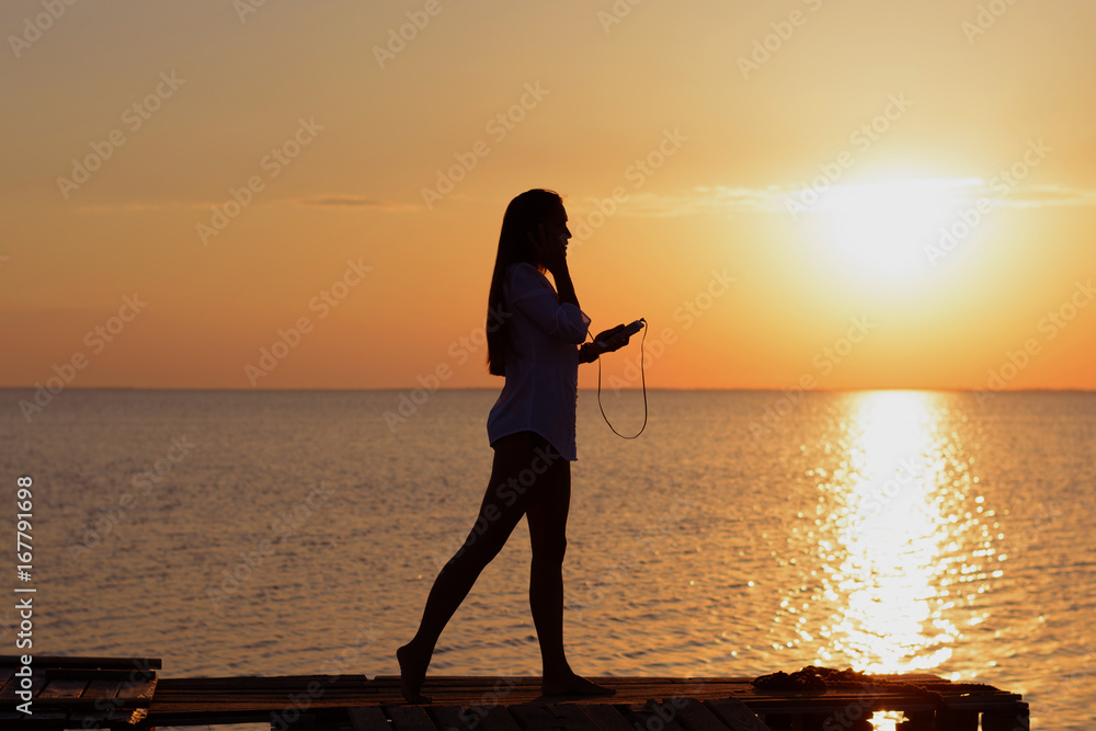Girl in headphones on a bridge by the sea
