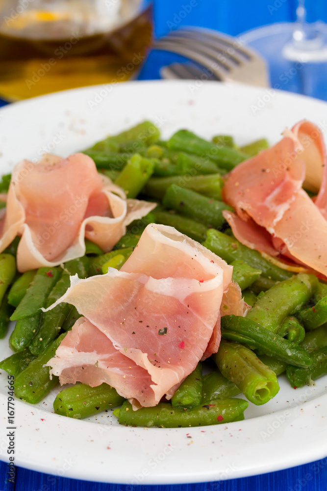 green beans with prosciutto on white plate on wooden background green beans with prosciutto on white plate on wooden background