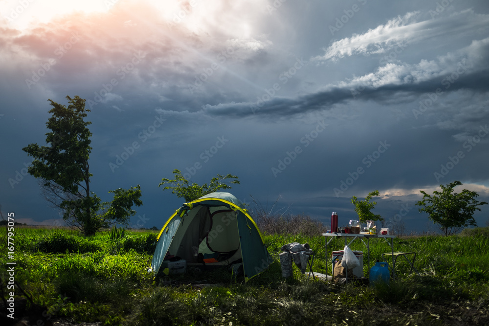 Tent set on the green lush meadow and stormy clouds on the background