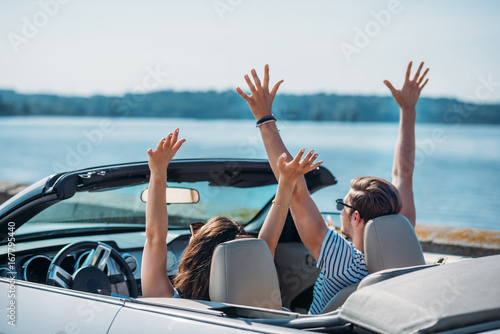 young couple with outstretched arms sitting in car together
