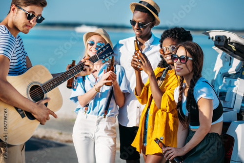 multiethnic group of friends drinking beer while spending time together at seaside