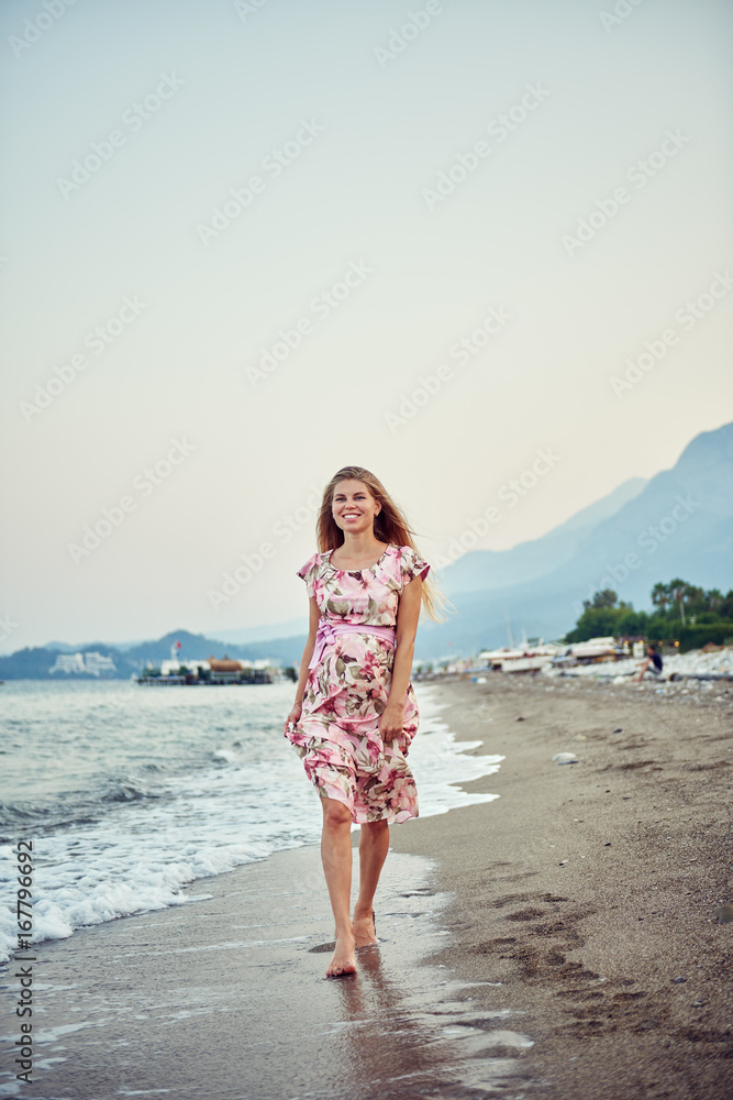 Young smiling pregnant female walking on the beach in the evening. 