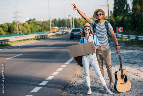 Konstfotografi young couple in love with empty cardboard hitchhiking while traveling together