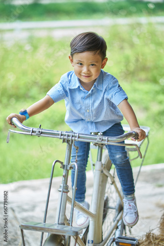 Asian boy sitting on an ancient bicycle.