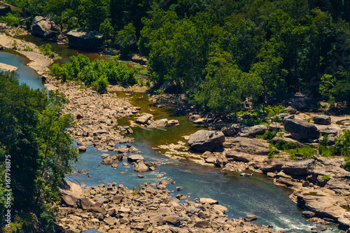 A rocky waterway visible from Hawks Nest State Park in southern West Virginia, with green trees surrounding it, and a few large stones nearby.