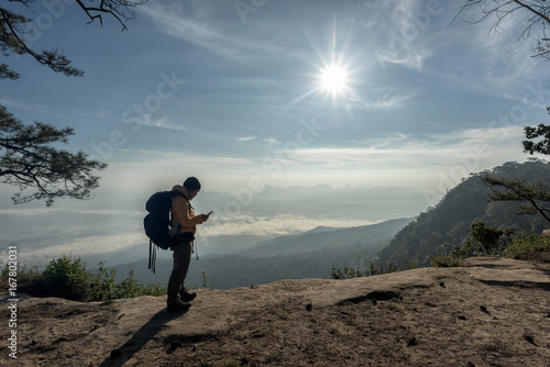 Traveler using mobile smart phone with backpack on cliff with beautiful landscape. Travel concept.