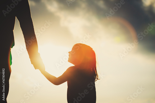 Murais de parede silhouette of little girl holding parent hand at sunset