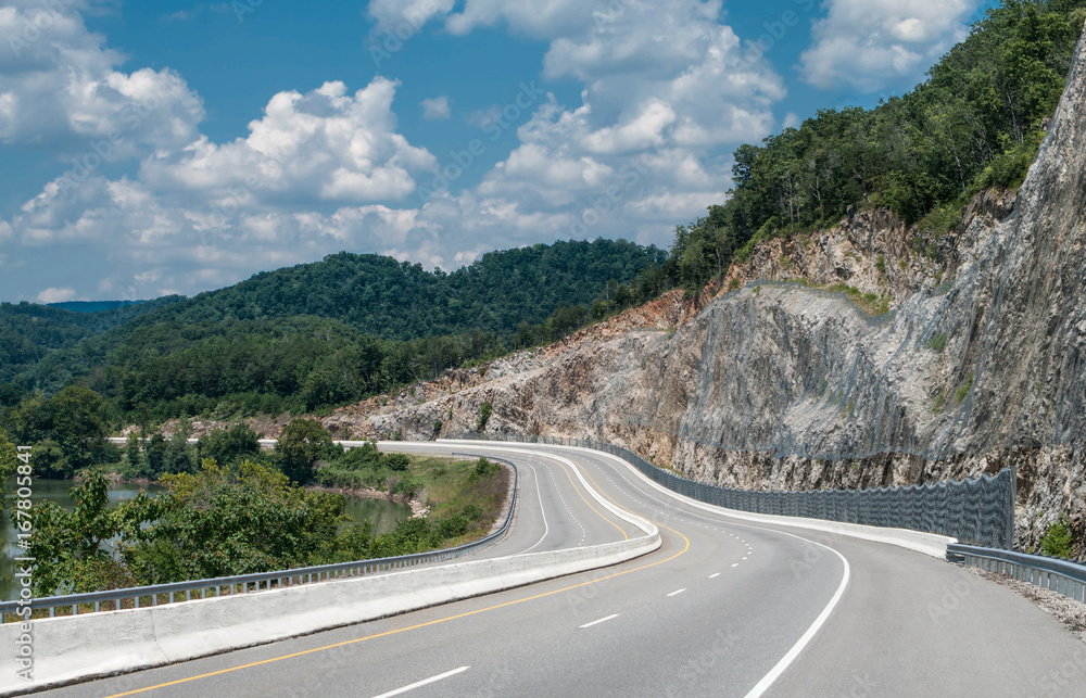 Appalachian Mountain Highway:  A four lane divided highway curves between a winding river and a steep cut rock face in eastern Tennessee.