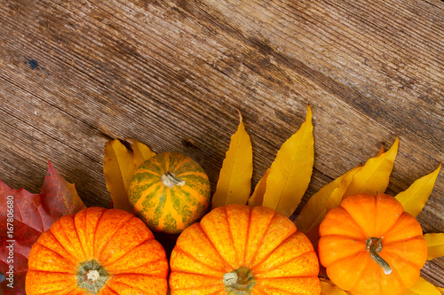 orange pumpkins with autumn leaves on wooden textured table close up