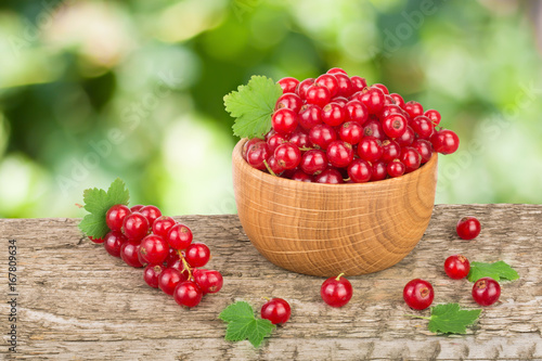 Red currant berries in wooden bowl on wooden table with blurry garden background
