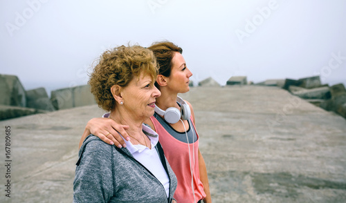 Senior and young sportswoman looking away by sea pier