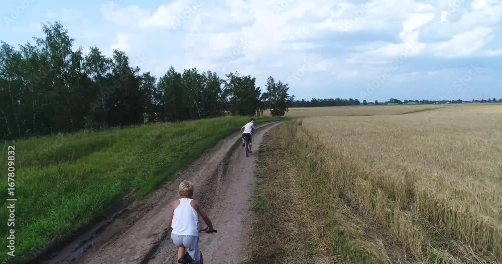 A young man with a child riding bicycles on a country road along the wheat fields. Shooting from a drone. Sports outdoors A young man with a child riding bicycles on a country road along the wheat fields. Shooting from a drone. Sports outdoors