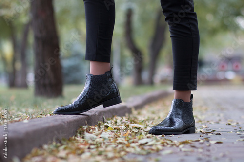 Python leather shoes. A girl steps in boots on an autumn foliage in a park