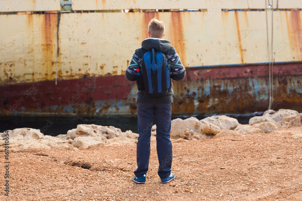 Male tourist looking at an abandoned ship on the sea or ocean back view. Adventure and tourism concept