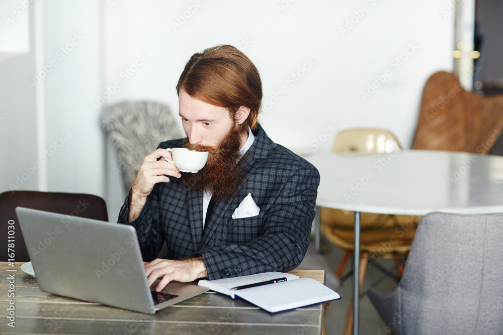 Young salresman drinking tea or coffee in cafe and looking through financial statistics online Young salresman drinking tea or coffee in cafe and looking through financial statistics online
