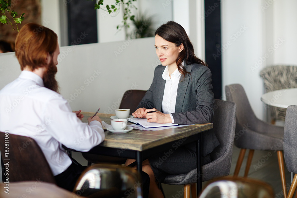Two young managers having discussion of business project at start-up meeting in cafe Two young managers having discussion of business project at start-up meeting in cafe