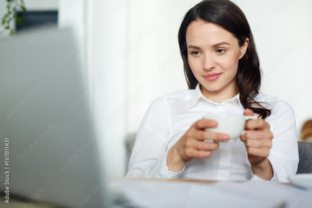 Businesswoman with cup of tea watching online video or talking through video-chat Businesswoman with cup of tea watching online video or talking through video-chat
