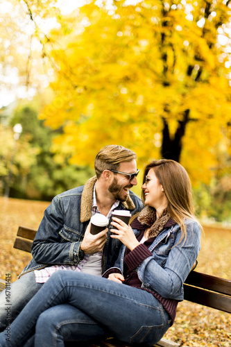 Young couple sitting on the bench with coffee cups in the autumn park