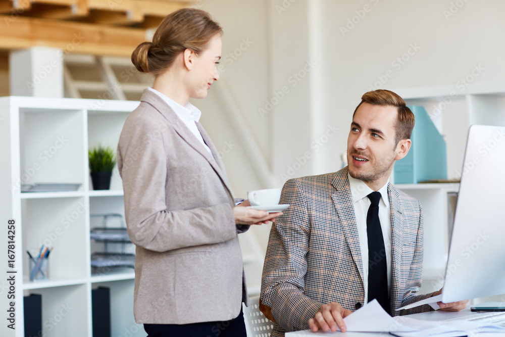 Pretty young woman with cup of fragrant coffee chatting animatedly with her handsome bearded colleague, interior of modern office on background Pretty young woman with cup of fragrant coffee chatting animatedly with her handsome bearded colleague, interior of modern office on background