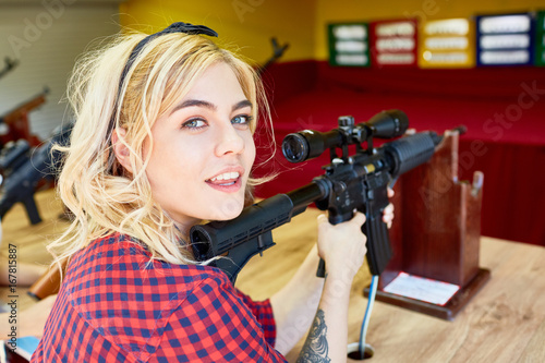 Cute teenage girl with rifle shooting at festival tent in amusement park