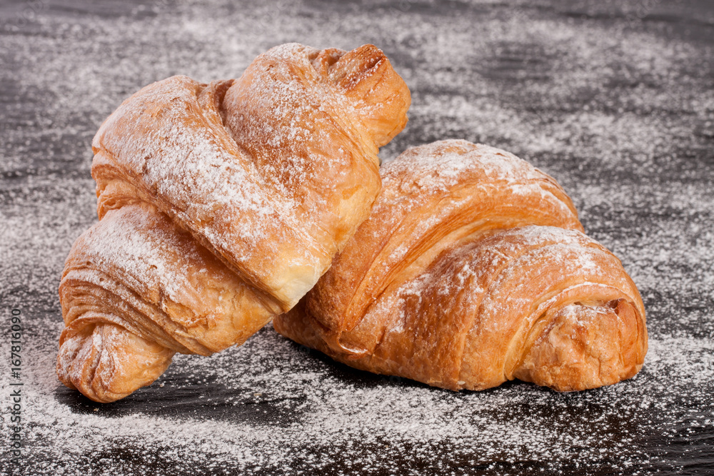 two croissant sprinkled with powdered sugar on black stone background closeup two croissant sprinkled with powdered sugar on black stone background closeup