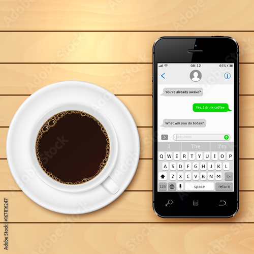 Mobile phone with sms chat on screen and coffee cup on wooden table