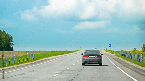 Rear view of a car speeding on asphalt road in countryside to escape summer thunderstorm.  Cloudy, stormy sky. Road signs along the route. © Eugene Put